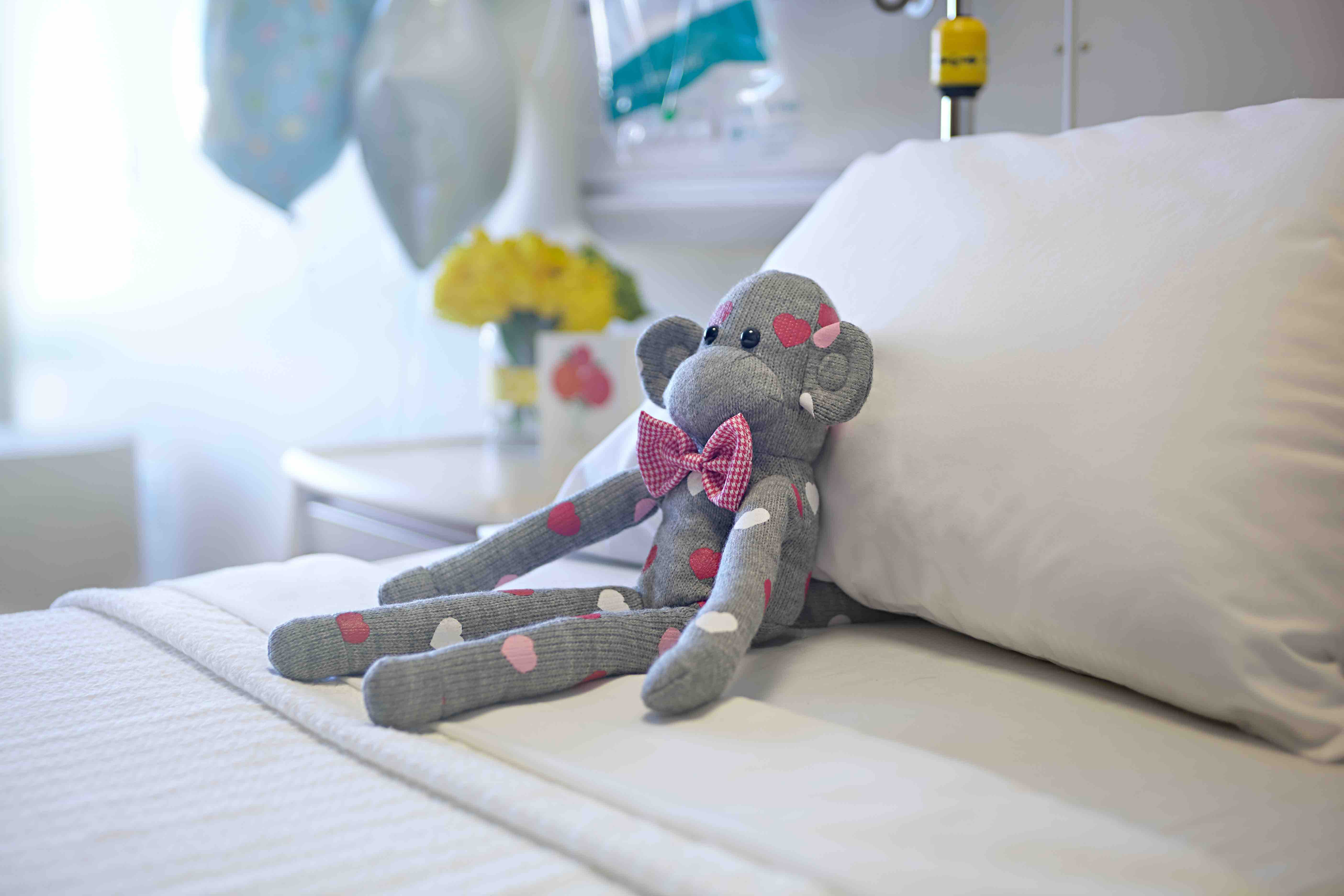 Gray monkey with a pink bowtie on a bed.