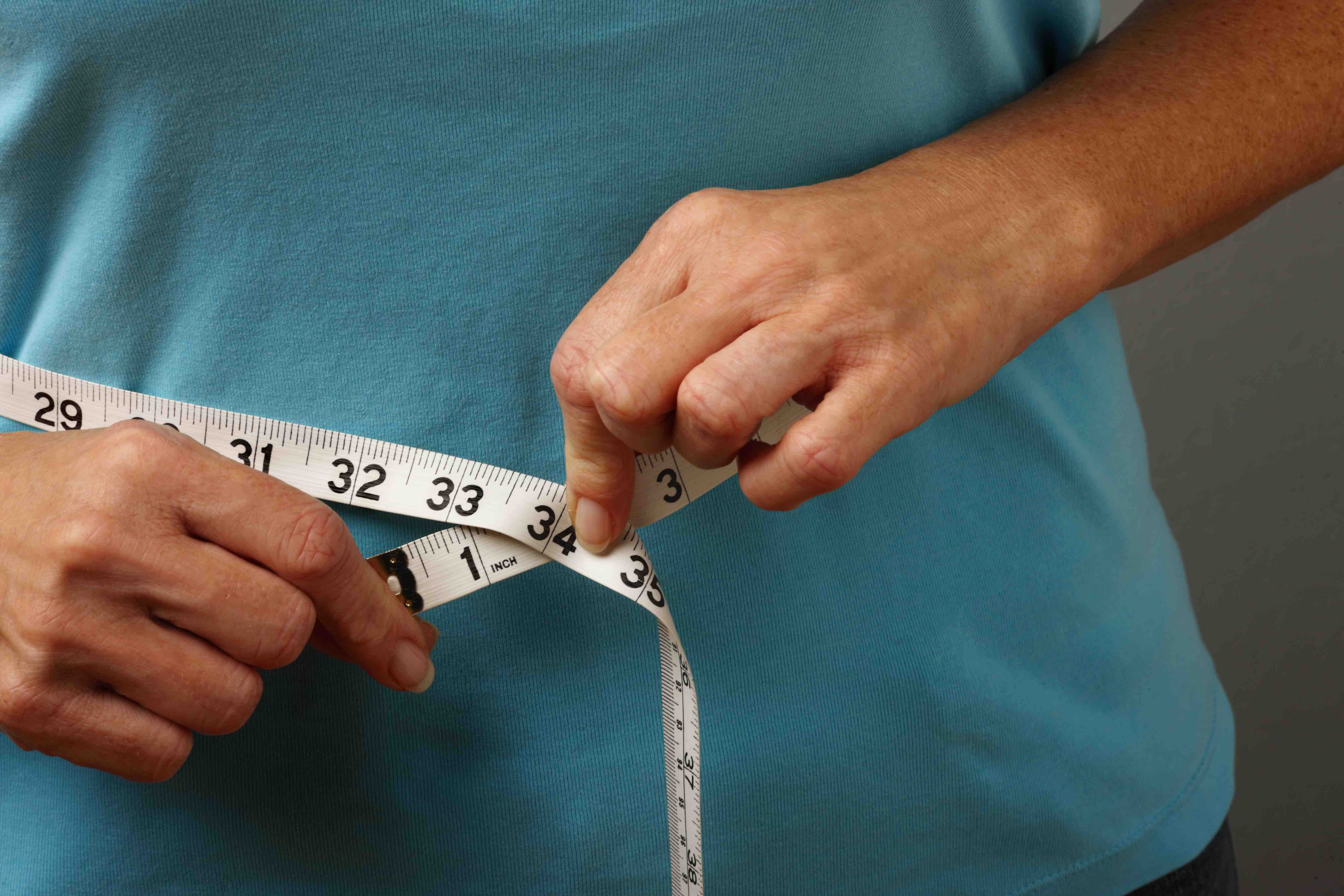 Person in blue shirt measuring waist size